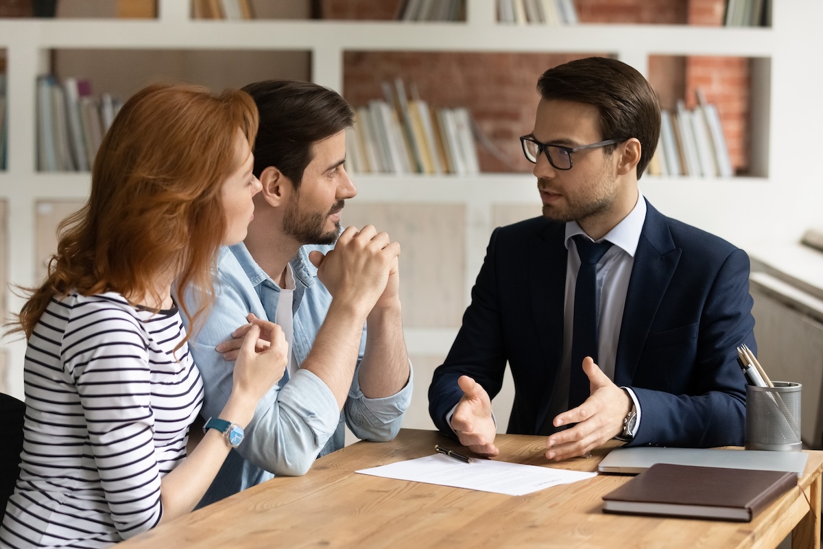 Professional male lawyer financial advisor consulting happy family couple clients in modern office. Interested young customers meeting Real Estate Agent broker bank worker, discussing agreement or deal.