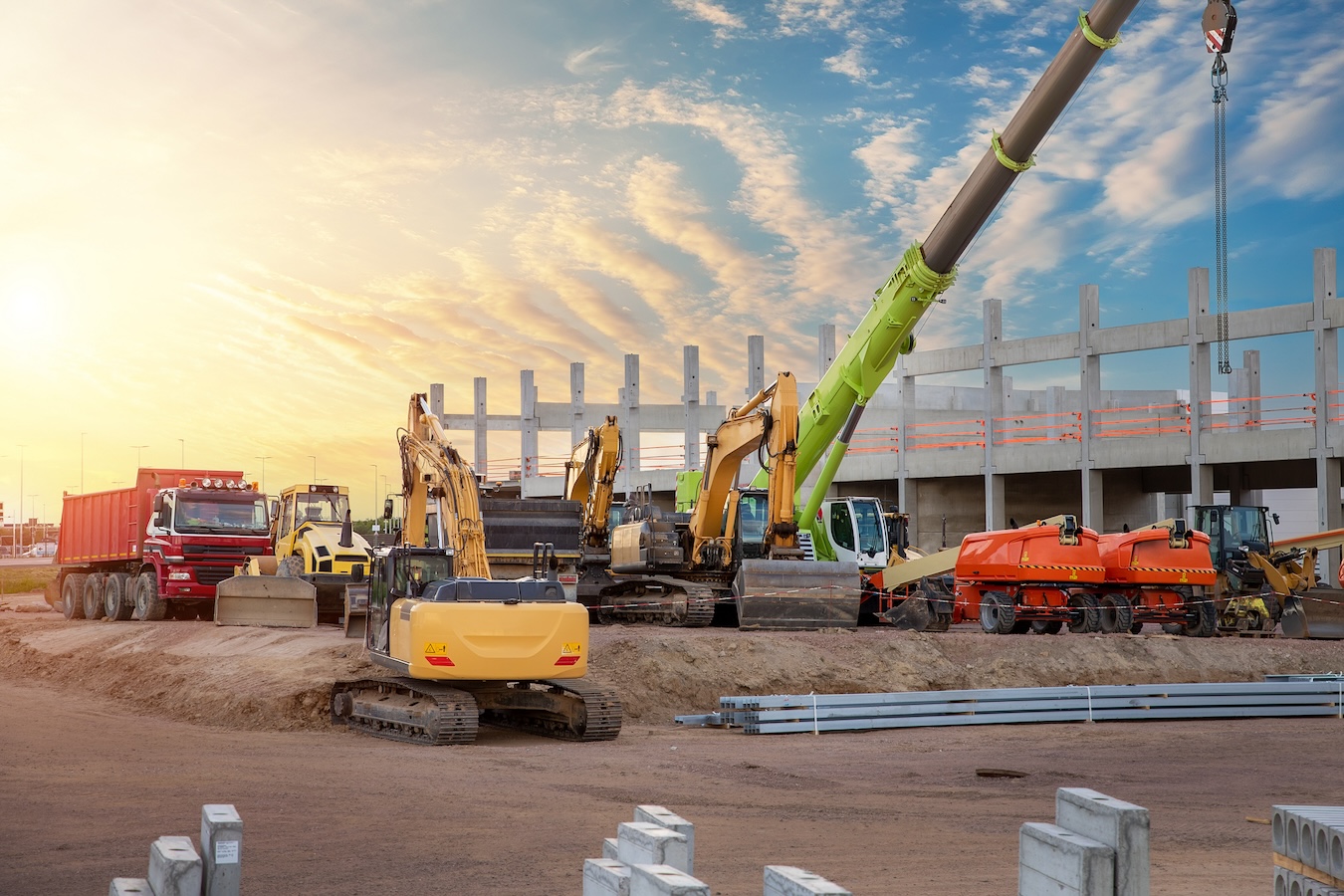 Many different multiclored colorful heavy industrial machinery equipment at construction site parking area against warehouse building city infrastructure development. Commercial vehicles rental sale.