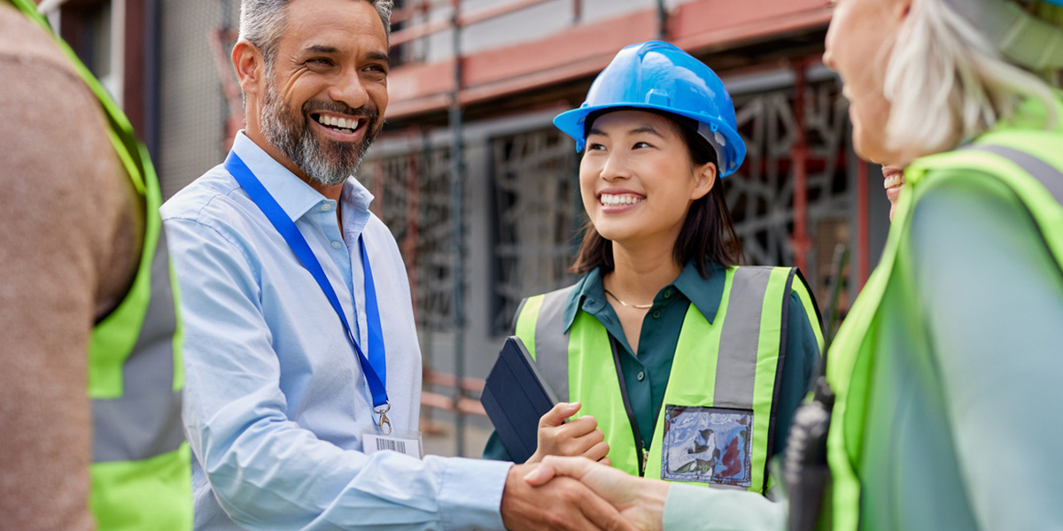 a woman in a hard had and safety vest is shaking hands with a man with an id lanyard